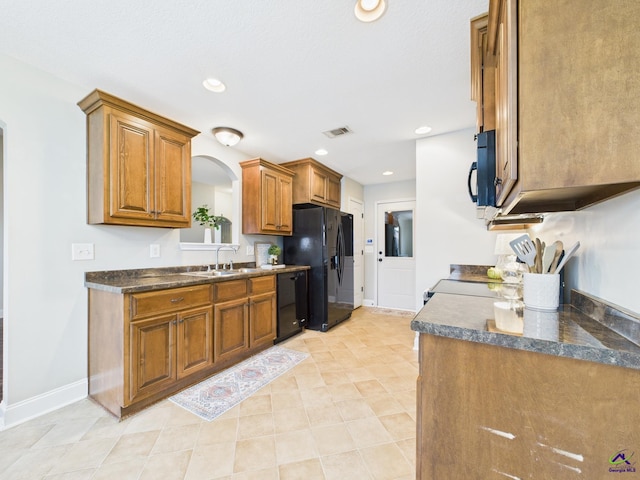 kitchen with dark countertops, baseboards, brown cabinets, black appliances, and a sink