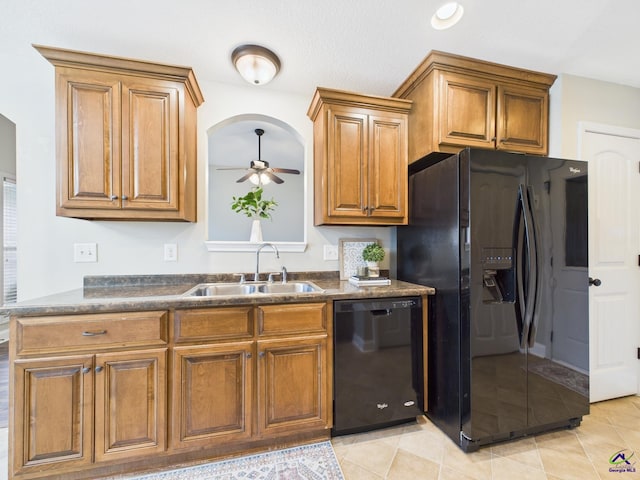 kitchen featuring a ceiling fan, brown cabinetry, a sink, black appliances, and dark countertops