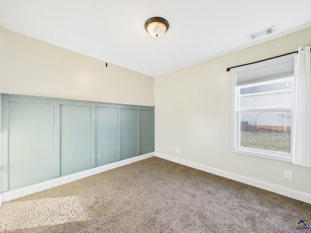 carpeted empty room featuring a wainscoted wall, a decorative wall, and visible vents