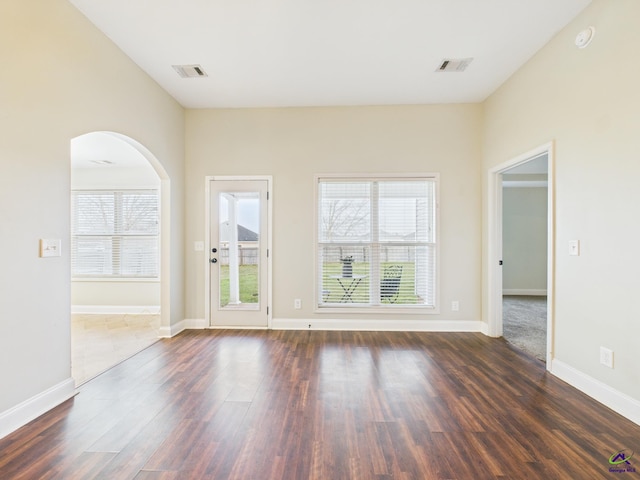 spare room with dark wood-style floors, visible vents, plenty of natural light, and arched walkways