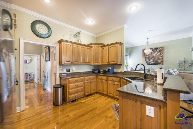 kitchen featuring dark stone countertops, light wood-style flooring, a sink, crown molding, and brown cabinets