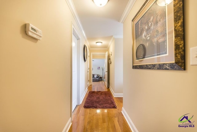 hallway featuring light wood-style flooring, crown molding, and baseboards