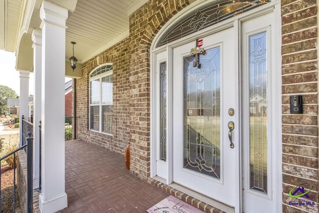 view of exterior entry featuring covered porch and brick siding