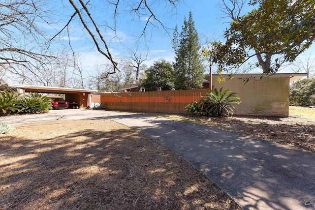 view of yard with a carport, concrete driveway, and fence