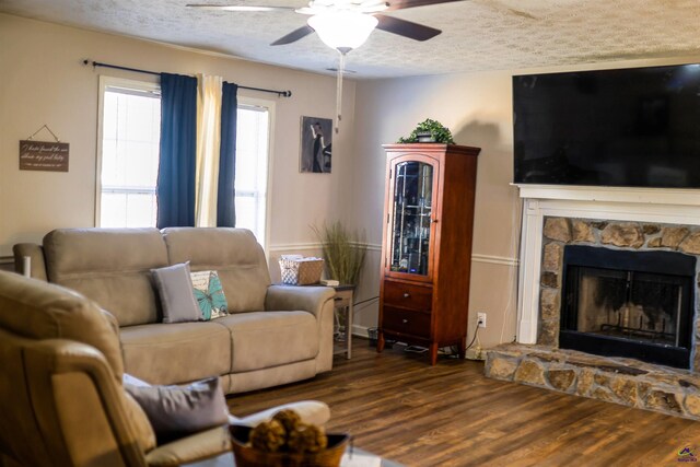 living room featuring a stone fireplace, a ceiling fan, wood finished floors, and a textured ceiling