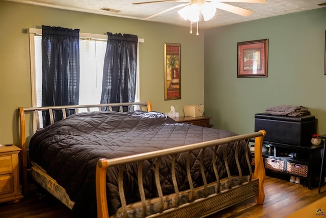 bedroom featuring dark wood finished floors, ceiling fan, visible vents, and a textured ceiling