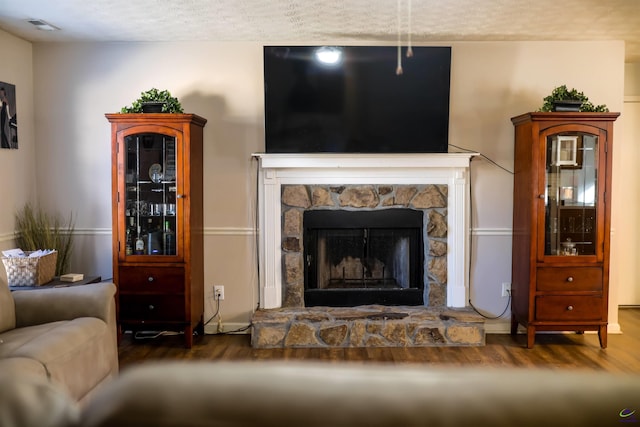 living area with visible vents, a textured ceiling, a stone fireplace, and wood finished floors