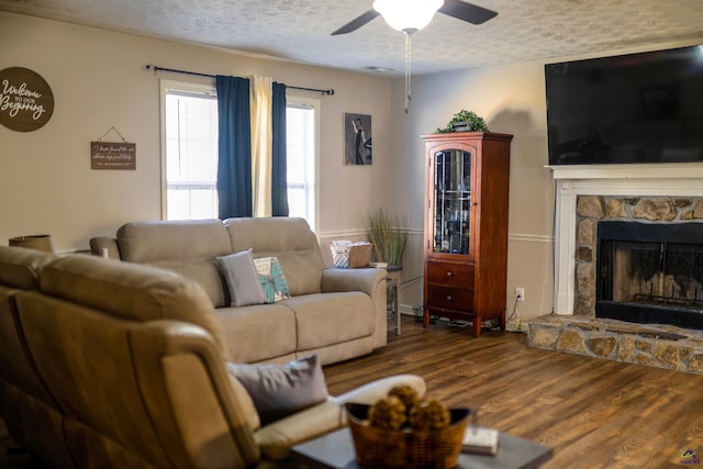 living area featuring a stone fireplace, ceiling fan, wood finished floors, and a textured ceiling