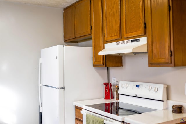 kitchen with under cabinet range hood, white appliances, brown cabinets, and light countertops