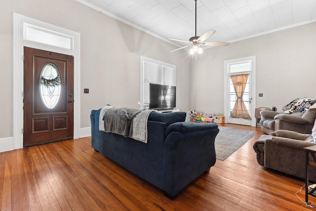 living area with baseboards, a ceiling fan, crown molding, and hardwood / wood-style flooring