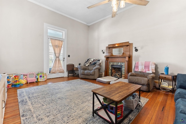 living room featuring wood-type flooring, ornamental molding, a ceiling fan, and a tile fireplace