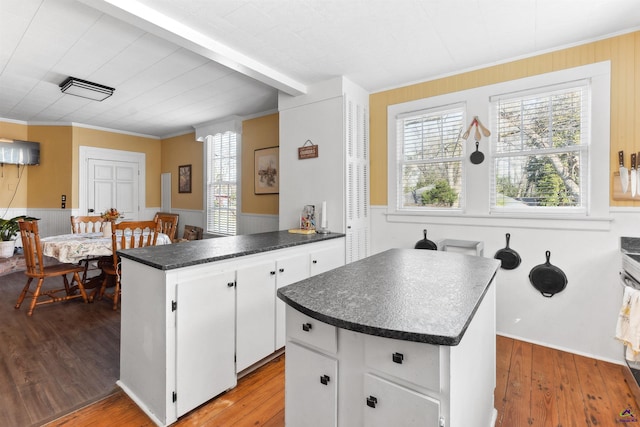 kitchen with dark countertops, a kitchen island, a peninsula, wood finished floors, and white cabinetry