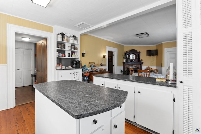 kitchen featuring dark countertops, white cabinets, a center island, and wood finished floors