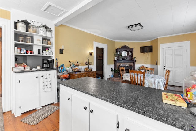 kitchen with dark countertops, a fireplace with raised hearth, ornamental molding, light wood-style flooring, and white cabinets