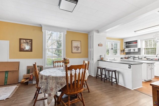 dining area with light wood finished floors, a wainscoted wall, and ornamental molding