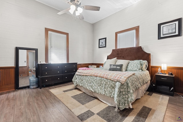 bedroom featuring light wood-type flooring, a wainscoted wall, ceiling fan, and wood walls