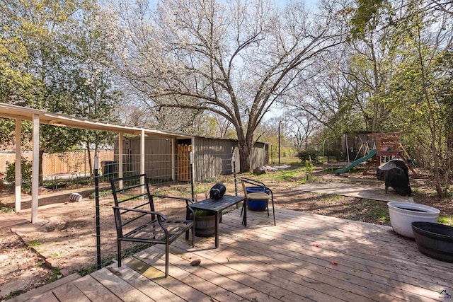 wooden terrace with a playground, fence, and grilling area