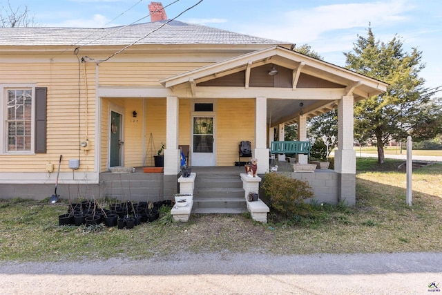 view of front of home featuring covered porch, roof with shingles, and a chimney