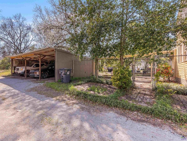 view of parking / parking lot featuring an outbuilding, a gate, fence, driveway, and a carport