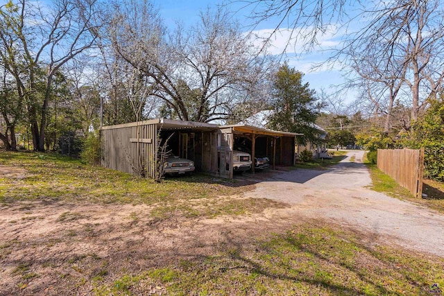 exterior space with a carport, fence, an outbuilding, and dirt driveway