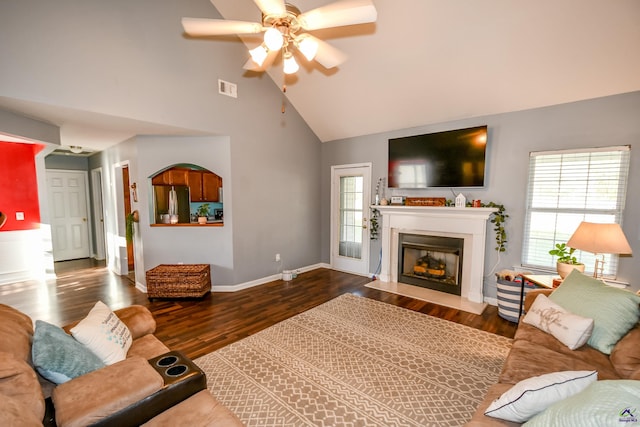 living area with visible vents, baseboards, a fireplace with flush hearth, wood finished floors, and high vaulted ceiling