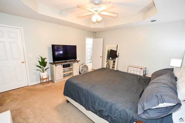 bedroom featuring visible vents, baseboards, a tray ceiling, light carpet, and a ceiling fan