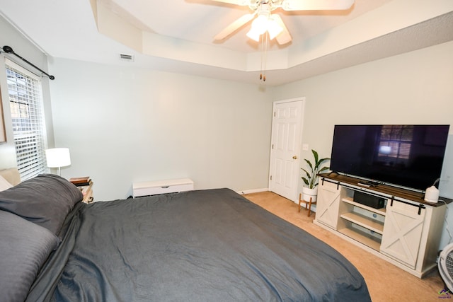 bedroom with a tray ceiling, light colored carpet, visible vents, and a ceiling fan