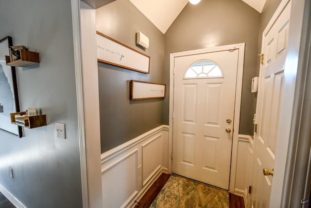 doorway featuring lofted ceiling, dark wood-style floors, wainscoting, and a decorative wall