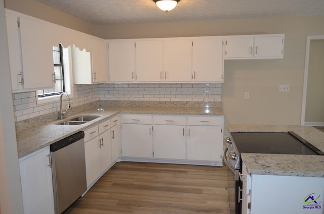 kitchen featuring wood finished floors, stainless steel appliances, decorative backsplash, a sink, and white cabinetry