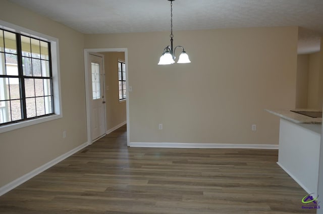 unfurnished dining area with baseboards, a textured ceiling, an inviting chandelier, and dark wood-style flooring