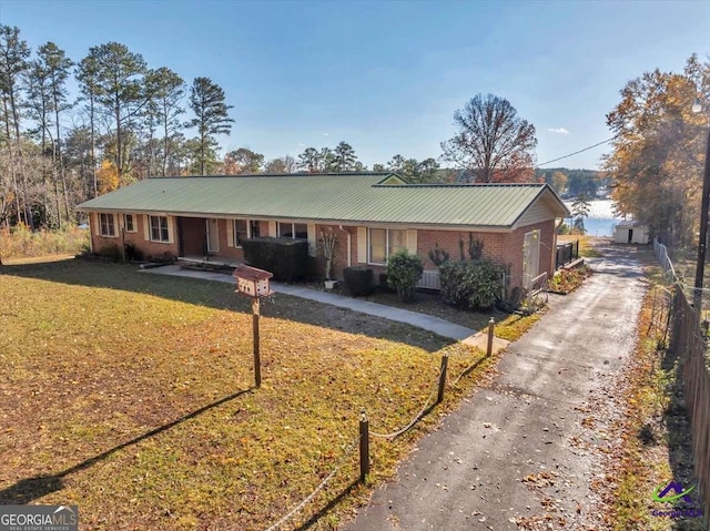 ranch-style house featuring driveway, covered porch, a front yard, metal roof, and brick siding