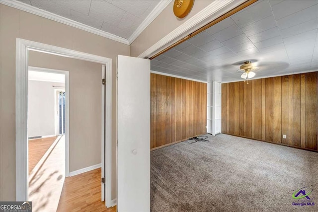 carpeted empty room with crown molding, baseboards, and wood walls