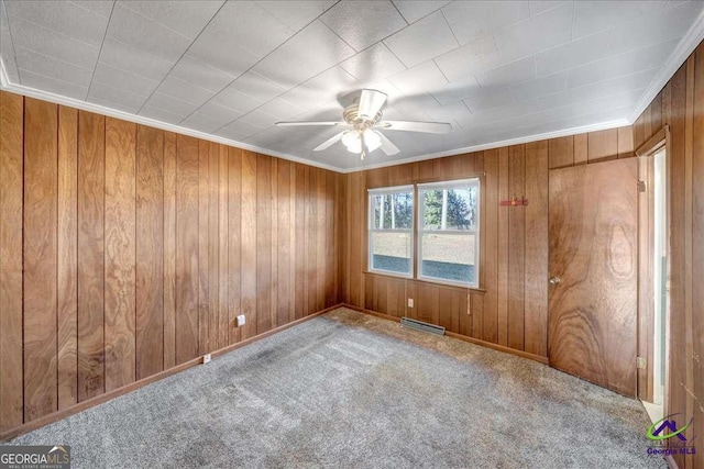 carpeted empty room featuring visible vents, ornamental molding, a ceiling fan, wood walls, and baseboards