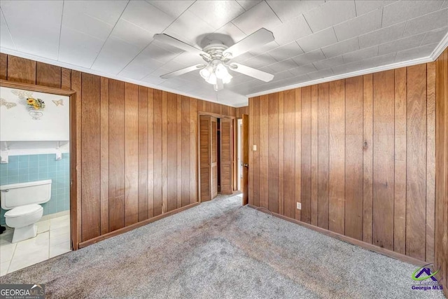 unfurnished bedroom with carpet floors, ceiling fan, tile patterned flooring, ensuite bathroom, and wood walls