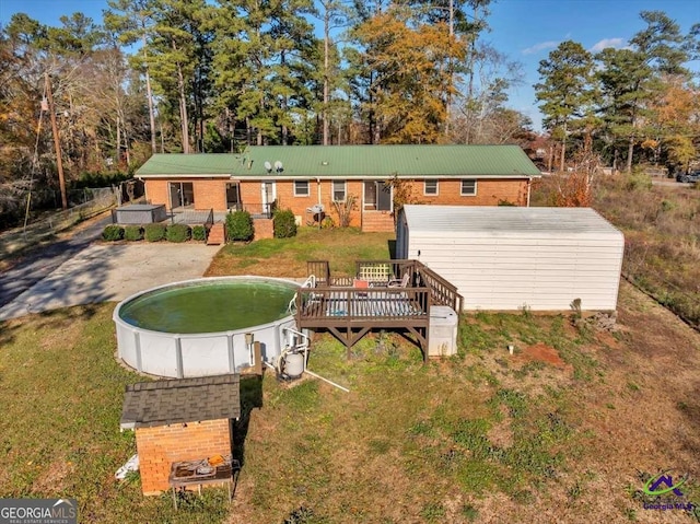 rear view of house featuring a wooden deck, a lawn, an empty pool, and brick siding