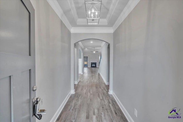 corridor with wood finished floors, baseboards, a tray ceiling, arched walkways, and ornamental molding