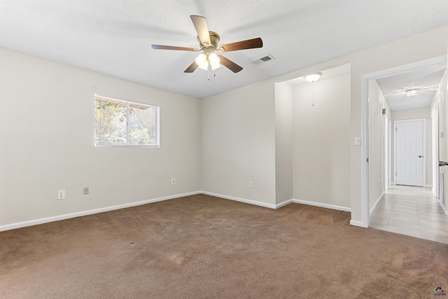 carpeted spare room featuring baseboards, a ceiling fan, visible vents, and a textured ceiling