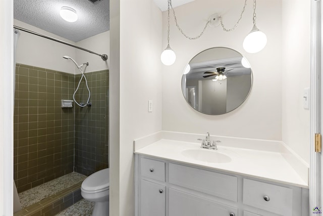 full bath featuring vanity, a ceiling fan, tiled shower, a textured ceiling, and toilet