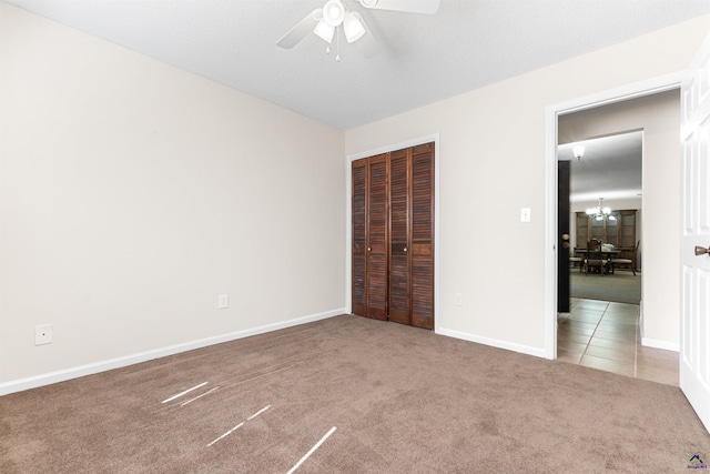 unfurnished bedroom featuring baseboards, a closet, carpet flooring, ceiling fan with notable chandelier, and tile patterned floors