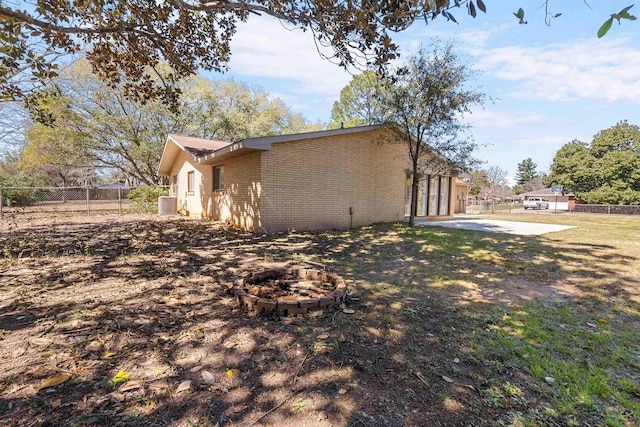 view of property exterior with fence, a yard, a fire pit, a patio area, and brick siding