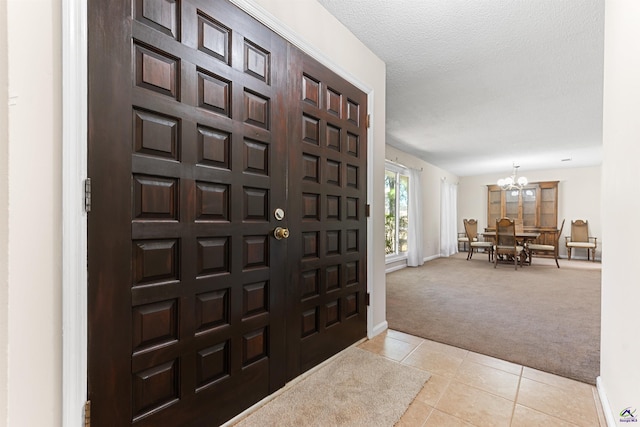 foyer with baseboards, a chandelier, light carpet, light tile patterned floors, and a textured ceiling