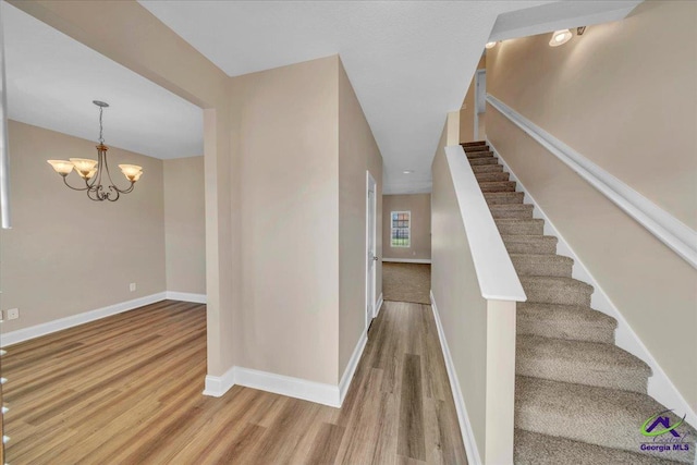 stairs with wood finished floors, baseboards, and a chandelier