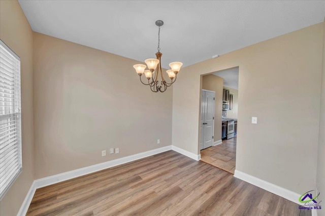 unfurnished room with baseboards, a notable chandelier, and wood finished floors