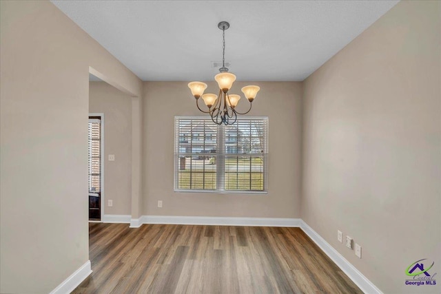 unfurnished dining area with visible vents, baseboards, an inviting chandelier, and wood finished floors