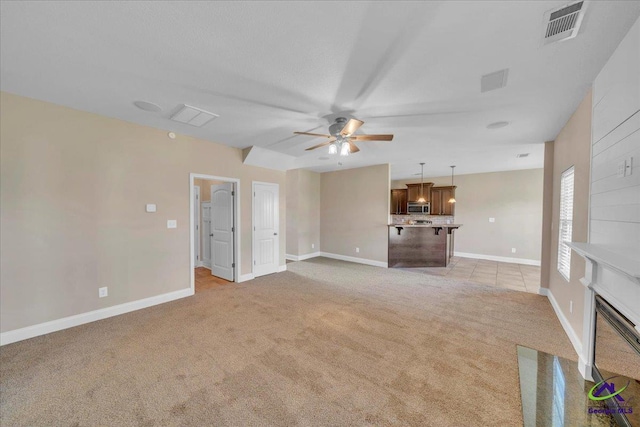 unfurnished living room featuring visible vents, baseboards, ceiling fan, a fireplace with flush hearth, and light colored carpet