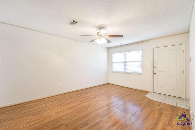 spare room featuring light wood finished floors, visible vents, a textured ceiling, and ceiling fan