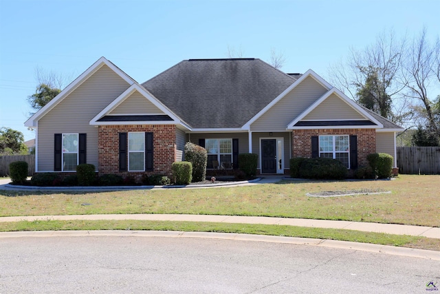 craftsman-style home with brick siding, a shingled roof, a front lawn, and fence