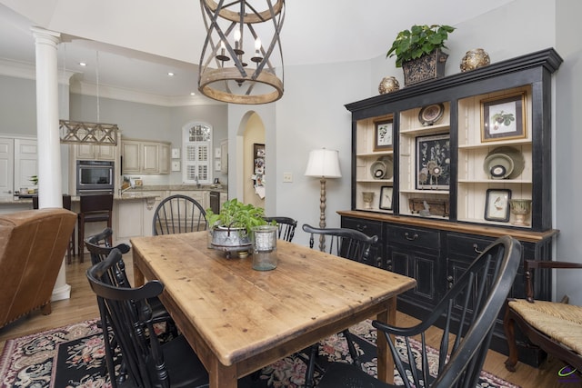 dining room with light wood finished floors, crown molding, decorative columns, recessed lighting, and arched walkways