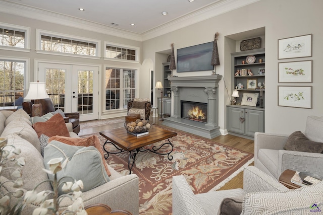 living area featuring built in features, wood finished floors, french doors, a glass covered fireplace, and crown molding