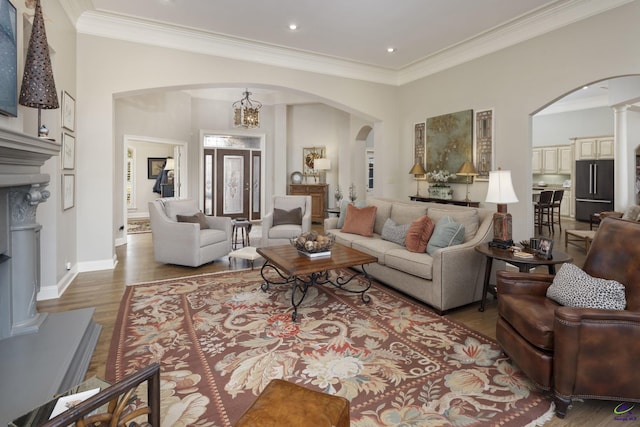 living area with ornamental molding, wood finished floors, arched walkways, baseboards, and a chandelier